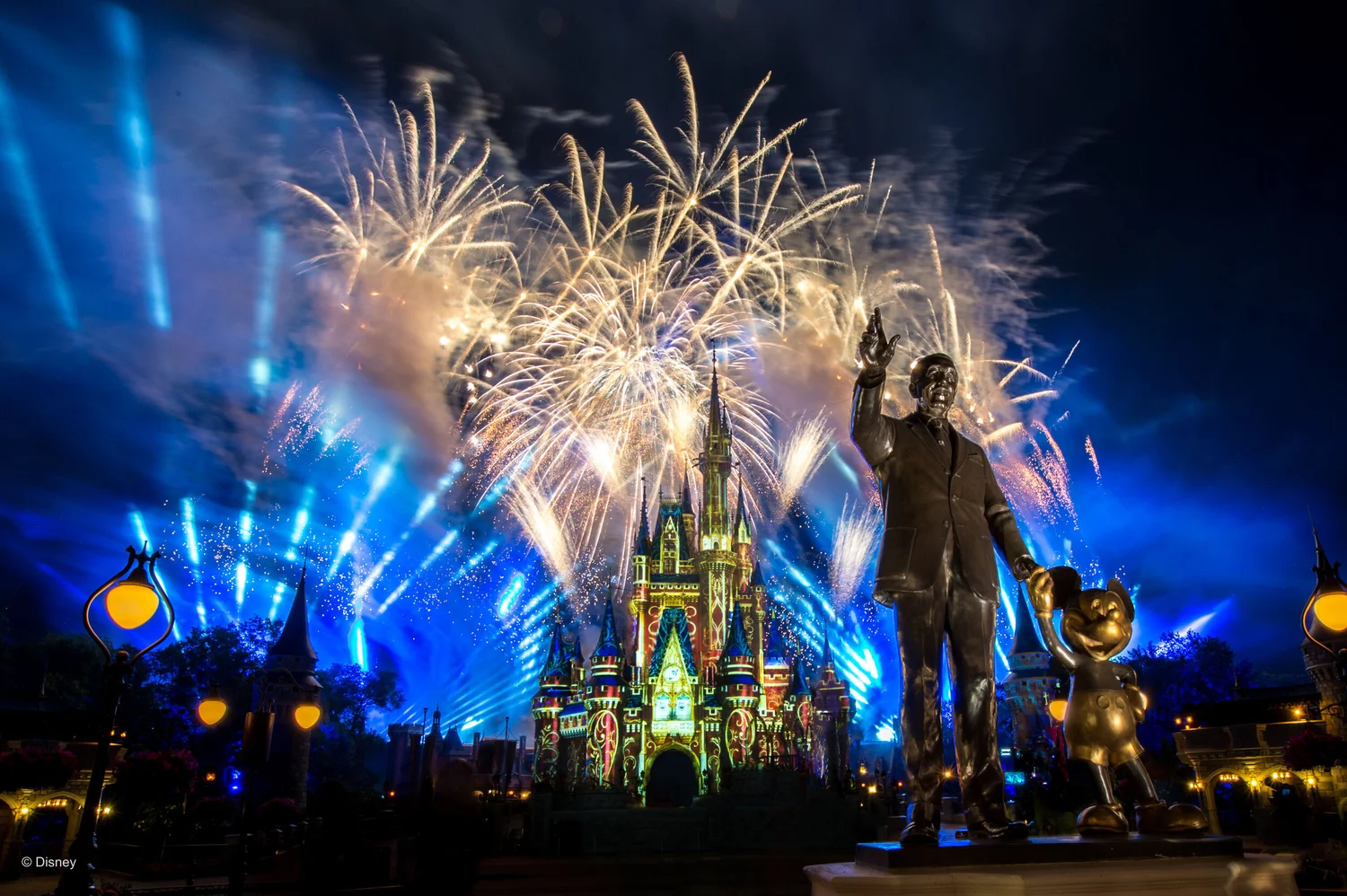 Walt Disney and Mickey Partners statue in front of Cinderella Castle with fireworks